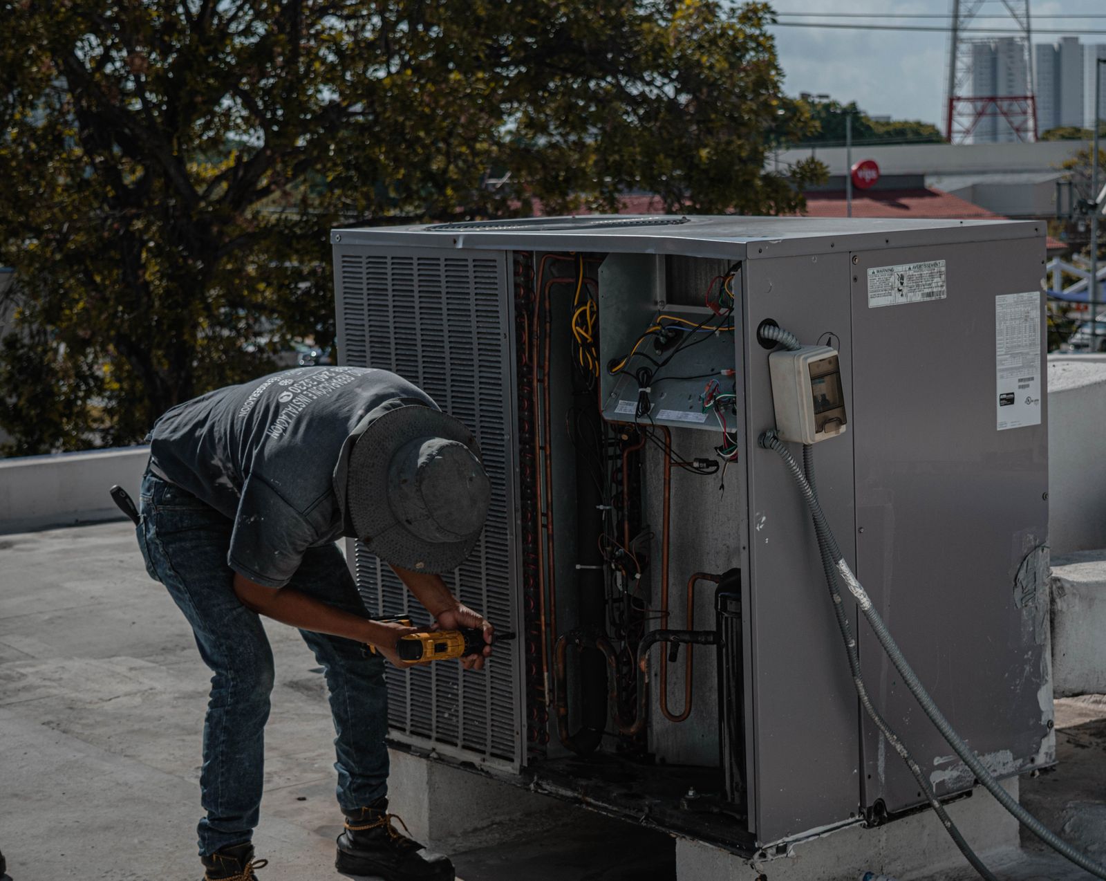 Um técnico está reparando uma unidade de ar condicionado em um telhado, demonstrando trabalho manual habilidoso.